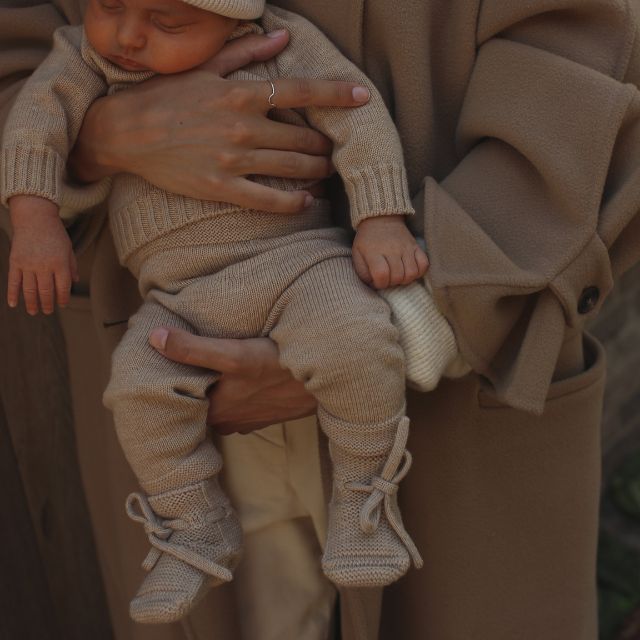 Hvid slofjes van merinowol sand aan bij een baby